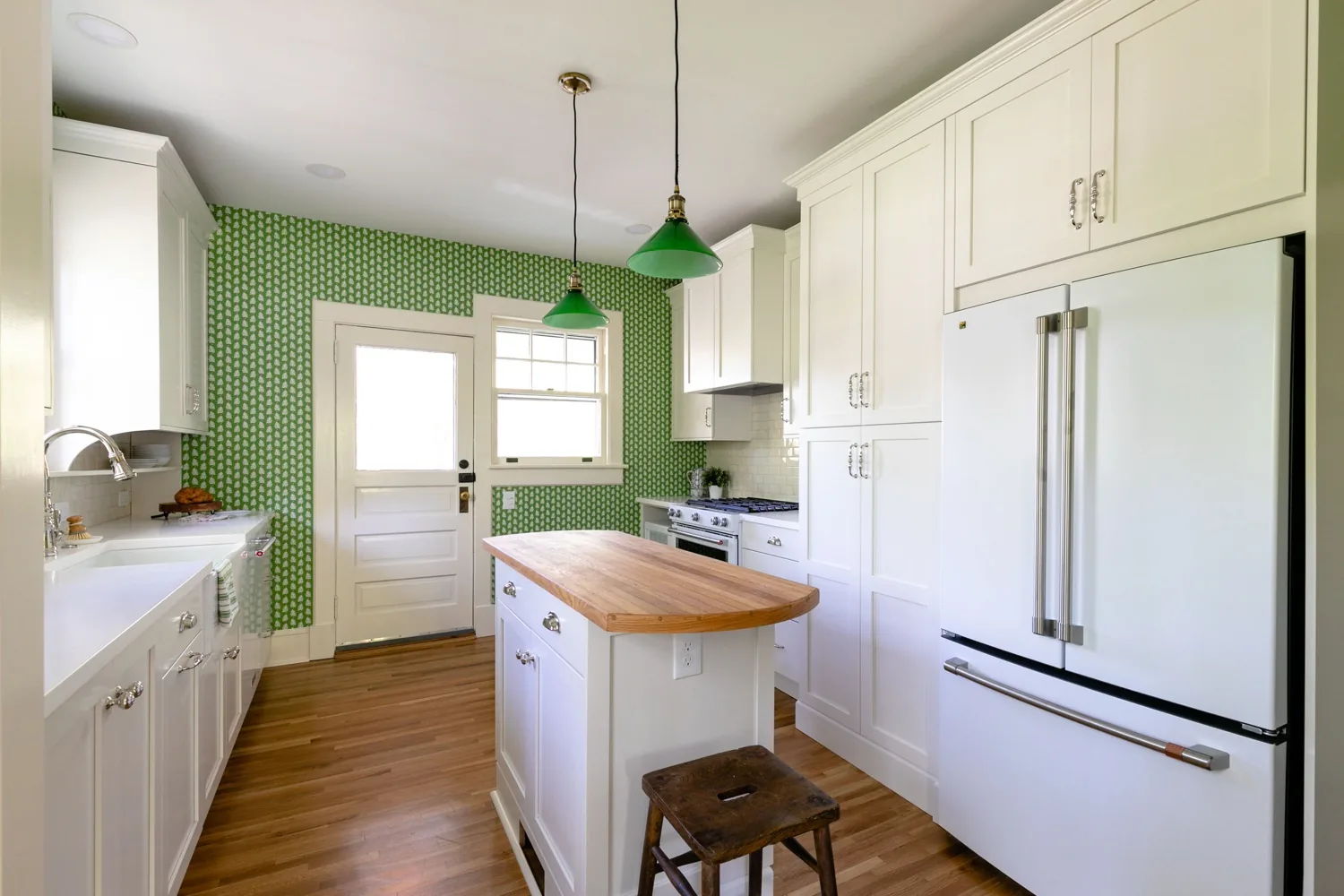 White kitchen with green patterned wallpaper, green pendant lights and a butcher block island