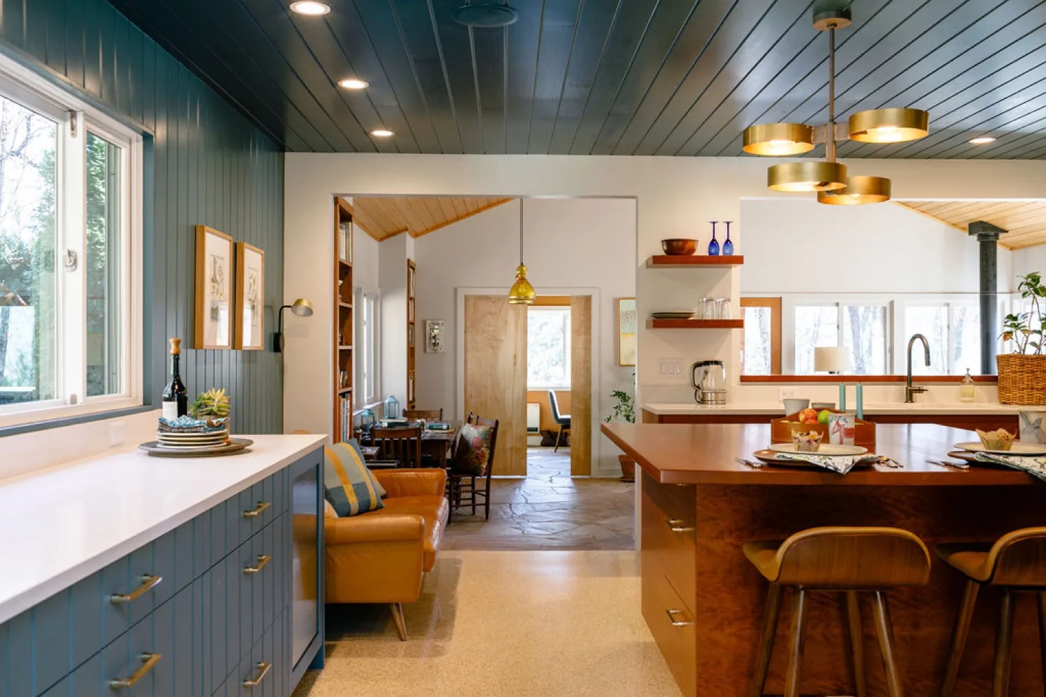 Open kitchen and living space with blue painted paneling, a wood island and brass pendants